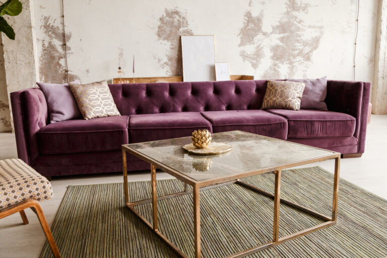 Purple velvet sofa with golden pillow in living room interior.