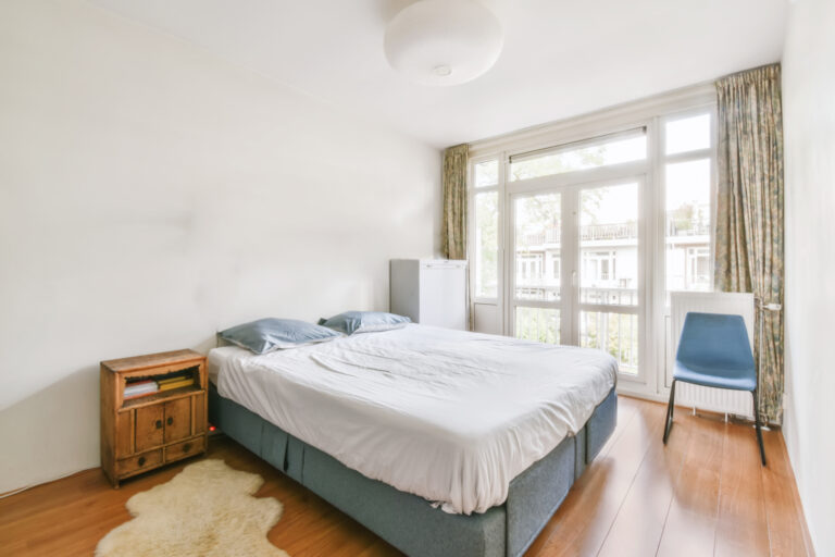 Comfortable bed covered with white blanket and located in light bedroom of modern apartment